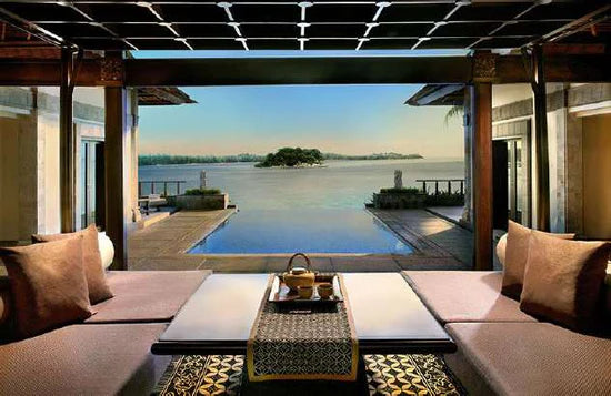 Luxurious open-air lounge with plush seating overlooks an infinity pool and serene lake with a small island in the distance, framed by elegant wooden architecture and soft natural lighting.